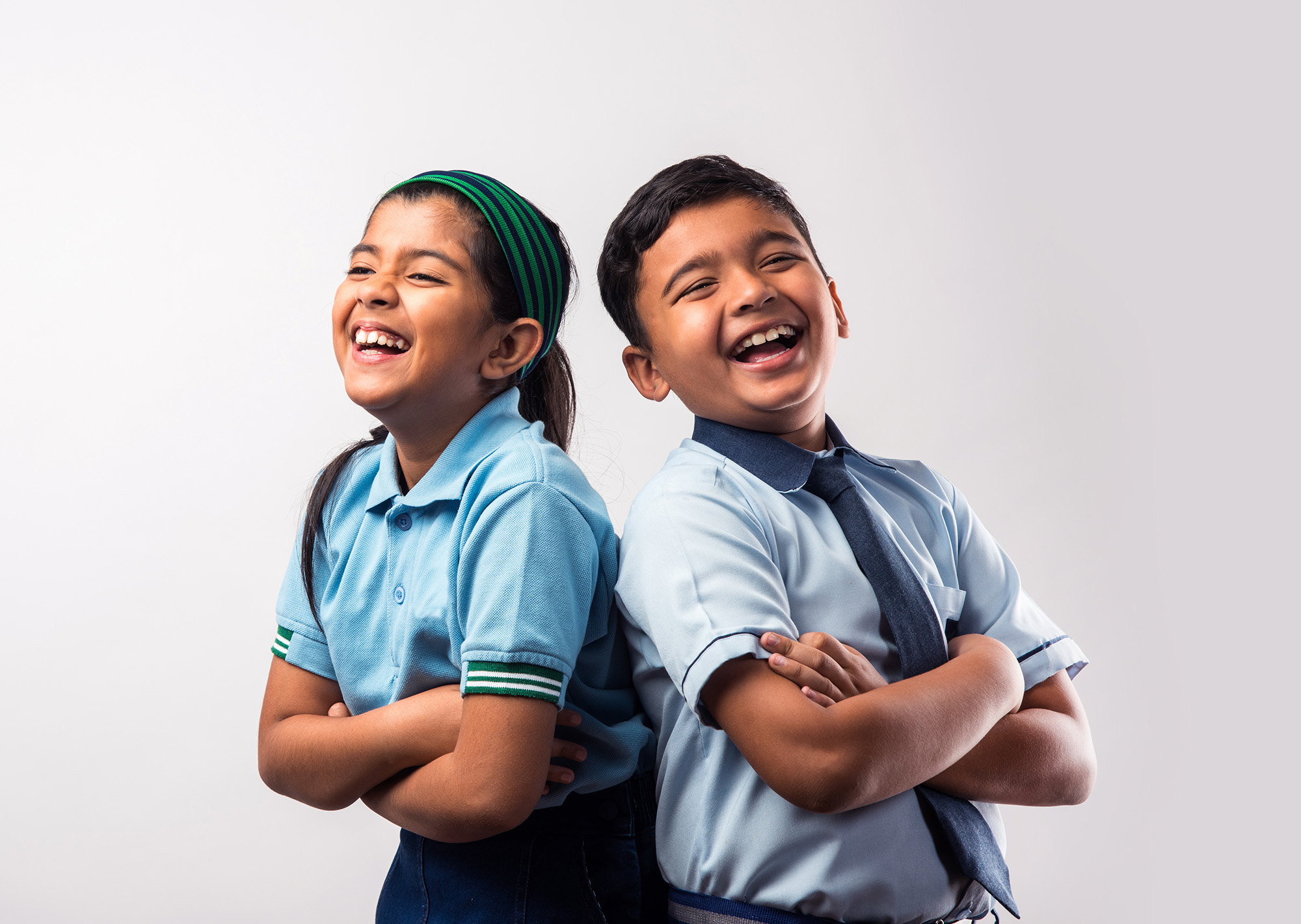 Young girl and boy students standing back to back smiling and laughing